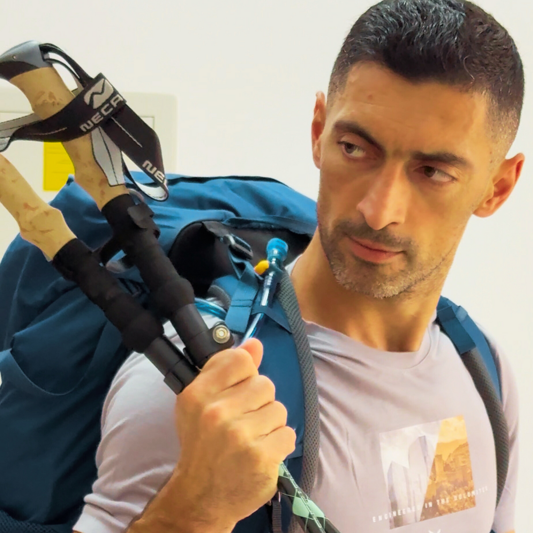 Edmond Margaryan holding two hiking poles in his left hand and looking at them, with blue hiking backpack on his shoulders